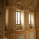 Percorriamo la scala lentamente con l'impressione di entrare "in un altro mondo": il silenzio sostituisce il vocio del viavai sottostante mentre ammiriamo le estese pareti che ci circondano, affrescate con cartigli e festoni dai colori essenzialmente beige e celeste